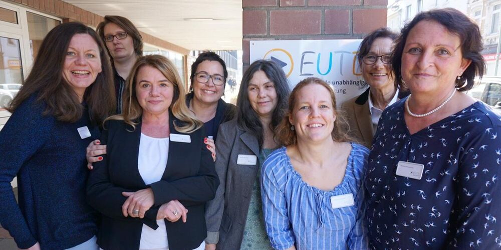 Mitarbeiterteam der Beratungsstelle. Dieses besteht aus acht Frauen, die in die Kamera lächeln und vor einem Vordach eines Gebäudes stehen. 